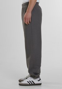 Pantalones de chándal de algodón grises con cintura elástica, tobillos ajustados y bolsillos laterales, combinados con zapatillas deportivas blancas y negras.