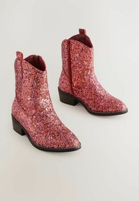Bottes à chevilles roses et paillettes avec un bout pointu, une fermeture éclair sur le côté et un petit talon empilé. Surface texturée avec des accents scintillants.