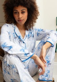 Pijamaset in lichtblauw en witte stof met palmbomen en zebra-patronen. Contrasterende blauwe piping langs de mouwen en de kraag.