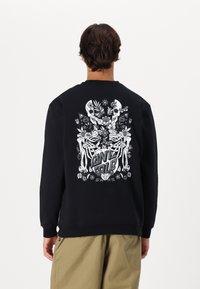 Zwarte sweatshirt met een grafische print op de achterkant met schedels, bloemen en de tekst "ANTIGOLD" in vette letters. Zacht, textured stof.