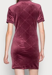 Velvet polo dress in burgundy, featuring a textured logo pattern, short sleeves, and a fitted silhouette. Smooth surface, subtle sheen.