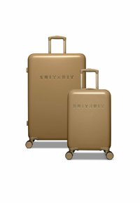 Twee gouden hard-shell koffers met het reliëf logo "SUITSUIT", uitgerust met uitschuifbare handvatten en vier wielen voor gemakkelijke mobiliteit.