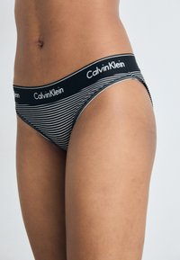 Black and white striped thong with a Calvin Klein logo waistband, made of soft fabric, featuring a low-rise cut and minimal coverage design.
