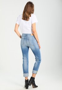 Jeans de mezclilla azul claro con corte recto, dobladillos enrollados y bolsillos traseros, combinados con una camiseta blanca básica y botas de tacón negras.