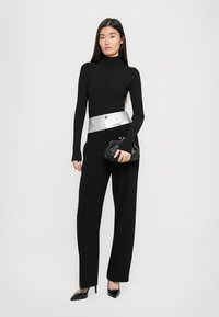 Pulover negru cu guler înalt, talie accentuată cu un curea argintie, pantaloni negri cu picior larg și geantă neagră. Modelul poartă tocuri negre cu vârf ascuțit.
