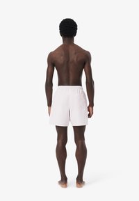 Shorts da bagno rosa chiaro con elastico in vita e tasca posteriore, realizzati in un tessuto liscio e leggero. Modello visto da dietro.