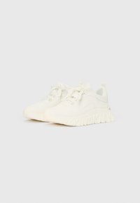 Λευκά αθλητικά παπούτσια με επάνω μέρος από υφασμάτινη υφή, στρογγυλεμένη μύτη, χοντρή σόλα με ανάγλυφο λογότυπο και κορδέλες για το κλείσιμο.