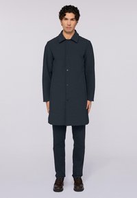 Tmavě modrý vlněný kabát s límcem, předním zapínáním na knoflíky a dlouhými rukávy, ve spojení s odpovídajícími kalhotami a hnědými koženými botami.