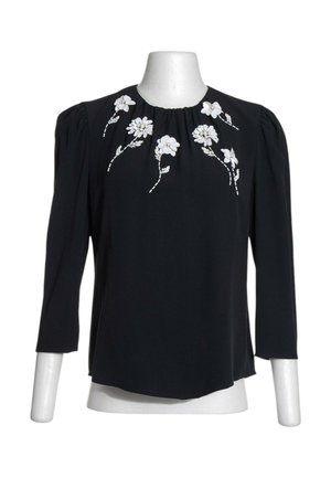 Blusa negra de manga larga con hombros abullonados y bordado floral blanco alrededor del escote sobre un maniquí blanco.