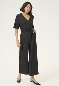 Svart jumpsuit med V-ringning, korta ärmar, framknappar och bälte i midjan. Har vida ben och en mjuk tygkvalitet.