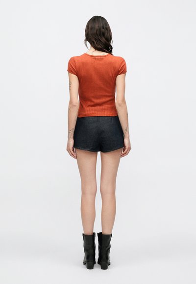Κοντομάνικη μπλούζα σε σκουριά απόχρωση με υφή, σετ με σκούρα τζιν σορτς και μαύρα μποτάκια αστραγάλου. Απλός, εφαρμοστός σχεδιασμός με στρογγυλή λαιμόκοψη.