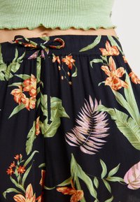 Schwarze Blumenhose mit leuchtend orangefarbenen und pinken Blumen, grünen Blättern und einem Kordelzug am Taillenbund. Aus leichtem Stoff gefertigt.