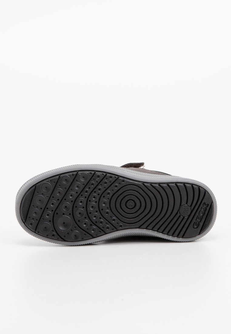 Semelle de chaussure en caoutchouc noir avec un motif de grip texturé, présentant des points et des rainures surélevés pour l'adhérence. Bord gris autour de la semelle.