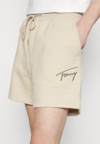 Shorts de algodón beige con cintura ajustable mediante cordón, bolsillos laterales y un logo de Tommy elevado en beige bordado en el muslo izquierdo.