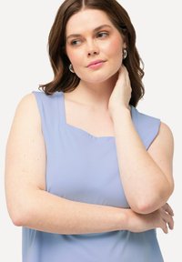 Lichtblauw mouwloos topje met een vierkante halslijn, gemaakt van een soepele stof. Opvallende details zijn het bijzondere schouderontwerp en de relaxte pasvorm.