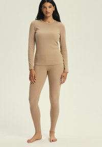 Beżowa bluzka z długim rękawem i dopasowane legginsy wykonane z gładkiego, elastycznego materiału. Strój ma okrągły dekolt i jednolitą teksturę.