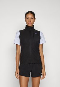 Zwarte vest met hoge kraag, volledige ritssluiting, textuurstof en een borstzak. Draag het over een grijze t-shirt en gecombineerd met zwarte shorts.