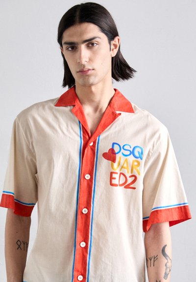 Chemise à manches courtes en coton beige avec un col et des poignets rouges. Présente un imprimé coloré : "DSQ VAR ED2" en bleu, jaune et rouge.