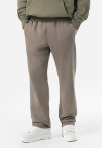Pantaloni de trening gri, confecționați dintr-un material moale, cu talie elastică, buzunare laterale și detalii discrete de branding. Asortați cu încălțăminte albă.