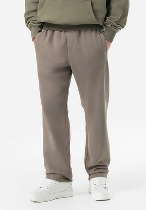 Pantaloni grigi in felpa realizzati in tessuto morbido con vita elastica, tasche laterali e dettagli di branding discreti. Abbinati a scarpe bianche.