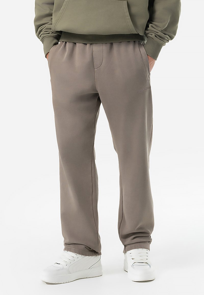 Pantaloni de trening gri, confecționați dintr-un material moale, cu talie elastică, buzunare laterale și detalii discrete de branding. Asortați cu încălțăminte albă.