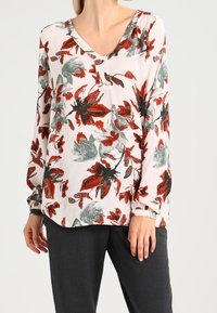 Long-sleeve blouse in light fabric, featuring a V-neck and a floral pattern with red, green, and black accents on a white background.
