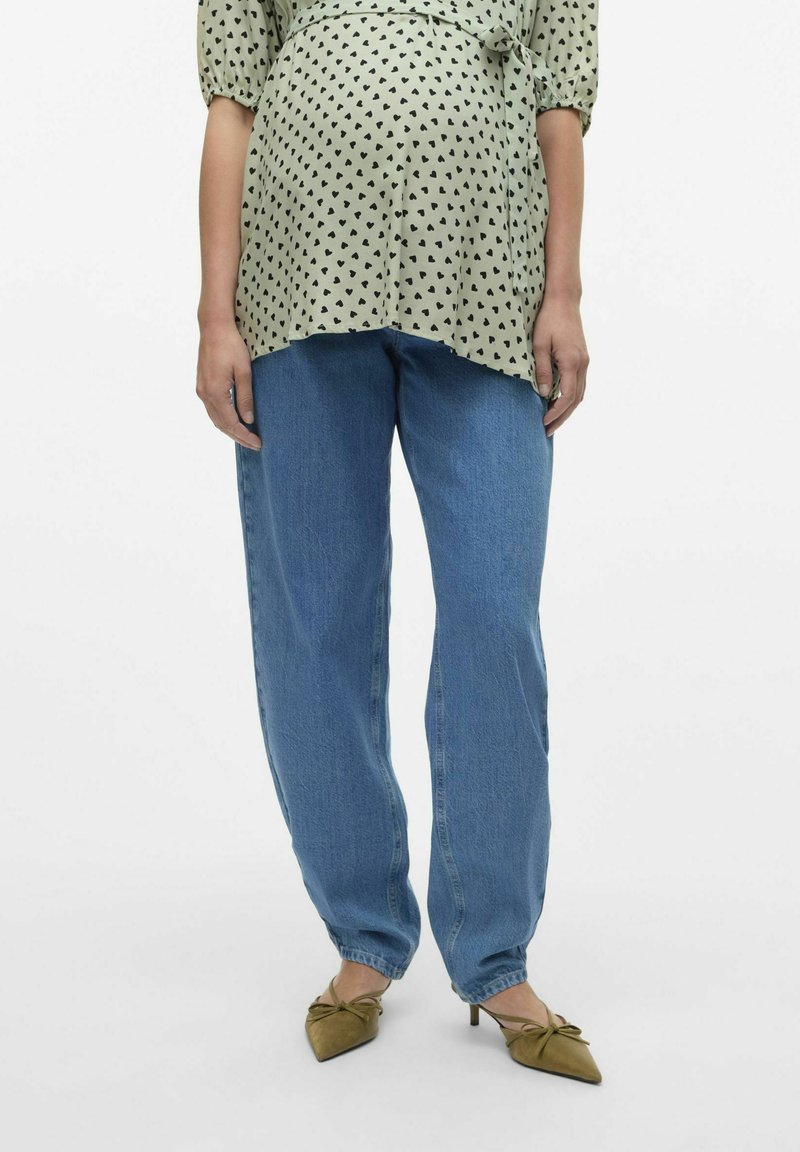 Blusa verde chiaro con stampa di cuori neri, abbinata a jeans blu dalla vestibilità ampia. Le scarpe punta di olive verde con dettagli a fiocco completano il look.