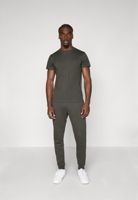 Olive green short-sleeve t-shirt paired with matching jogger pants, both in a smooth cotton blend. White sneakers complete the outfit.