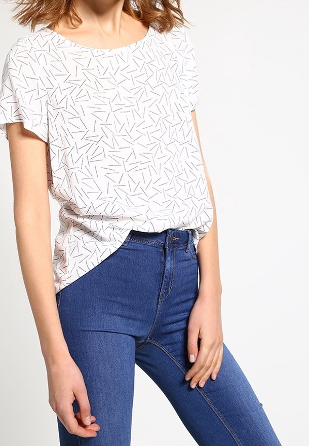 Haut blanc à manches courtes avec un motif de lignes noires dispersées, associé à un jean bleu taille haute. Coupe décontractée, texture lisse.