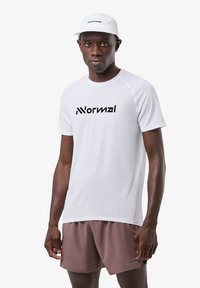 Weißes, leichtes Sportshirt aus strukturiertem Stoff, mit kurzen Ärmeln und schwarzem Logo. Getragen mit braunen Shorts und einer passenden weißen Kappe.