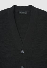 Cardigan noir avec un motif en tricot texturé, col en V, et cinq boutons sur le devant. L'étiquette indique "CALLIOPE", taille L.