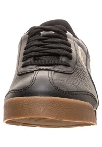 Svart lädersneaker med svarta snörningar och en texturerad ljusbrun gummisula, visad från en närbild framifrån.