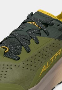 Baskets de sport vertes avec tige en mesh, accents jaunes et lacets noirs. Présente des détails perforés et une semelle en caoutchouc texturée.