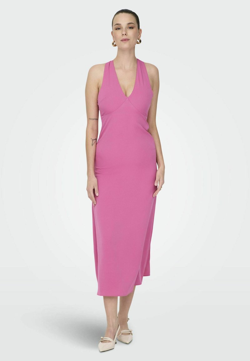 Roza halter obleka v prilegajočem dizajnu, izdelana iz gladkega materiala, z globokim V-izrezom in dolžino do tal, v kombinaciji s bež čevlji.