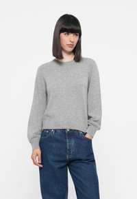 Suéter de lana gris con un cuello redondo y mangas largas, ligeramente abullonadas, combinado con jeans de denim azul oscuro. Diseño simple y limpio.