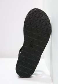 Sola di sandalo nera con superficie texturizzata caratterizzata da un motivo a diamante e il logo "Teva". Il materiale appare gommoso e flessibile.