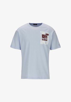 T-shirt en coton bleu clair avec col rond, manches courtes, motif sur la poche avant représentant des palmiers et du texte en bordeaux et blanc.