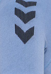 Jasnoniebieska bluza z teksturowanym wykończeniem, z czarnym nadrukowanym wzorem w zygzak na górnej części. Miękki, casualowy materiał.