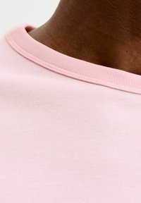 Hellrosa Baumwoll-T-Shirt mit geripptem Rundhalsausschnitt, glatter Textur und sichtbaren Nähten entlang des Kragens.