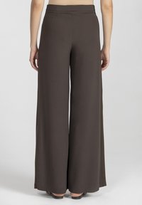 Szerokie, brązowe spodnie wykonane z gładkiego materiału; posiadają dopasowaną talię i brak widocznych kieszeni, z długością do podłogi.