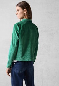 Grøn kordfløjljakke med en klassisk krave og knapmanchetter, parret med mørkeblå denim. Har en struktureret overflade og en afslappet pasform.