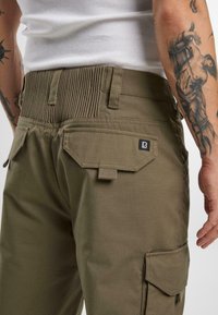 Pantalones cargo color caqui con una cinturilla acanalada, dos bolsillos traseros y una etiqueta de logo negra. Fabricados con un tejido texturizado y duradero.