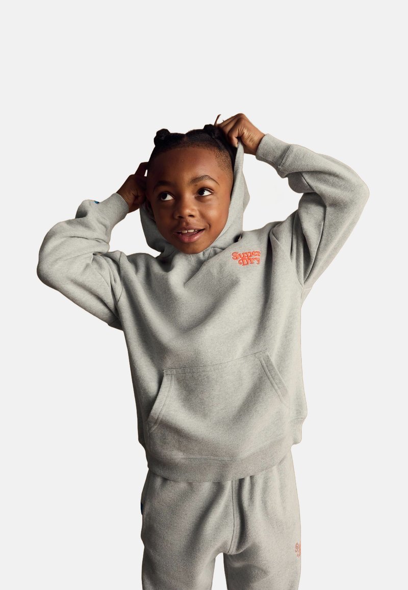 Sudadera gris con un bolsillo frontal y pantalones de chándal a juego. Presenta un logotipo naranja. Tejido suave y texturizado; ajuste holgado.