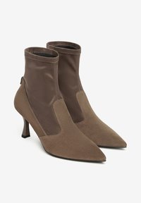 Stivaletto marrone a punta con finitura in morbida pelle scamosciata e tomaia in tessuto elastico, dotato di un tacco basso e ritagli laterali per un contrasto di design.