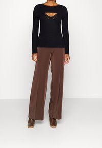 Pull noir à manches longues côtelé avec un décolleté découpé, associé à un pantalon large marron et des bottines marron.