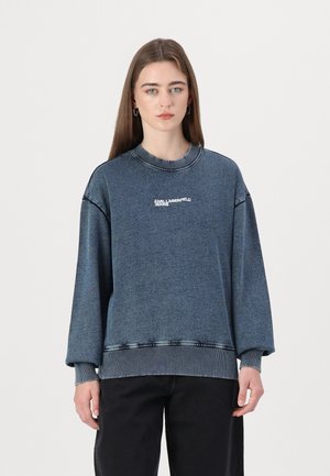 Felpa in denim blu con polsini e orlo a costine, caratterizzata da una stampa bianca del logo. Vestibilità ampia con dettagli di cucitura in evidenza.