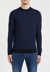 Pull en maille bleu marine avec motif texturé, col rond, manches et ourlet côtelés, associé à un jean en denim bleu.