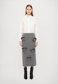 Fustă gri cu patru ecusoane decorative la guler și nasturi, asortată cu o cămașă albă cu mâneci lungi. Boots negre până la glezne completează ținuta.