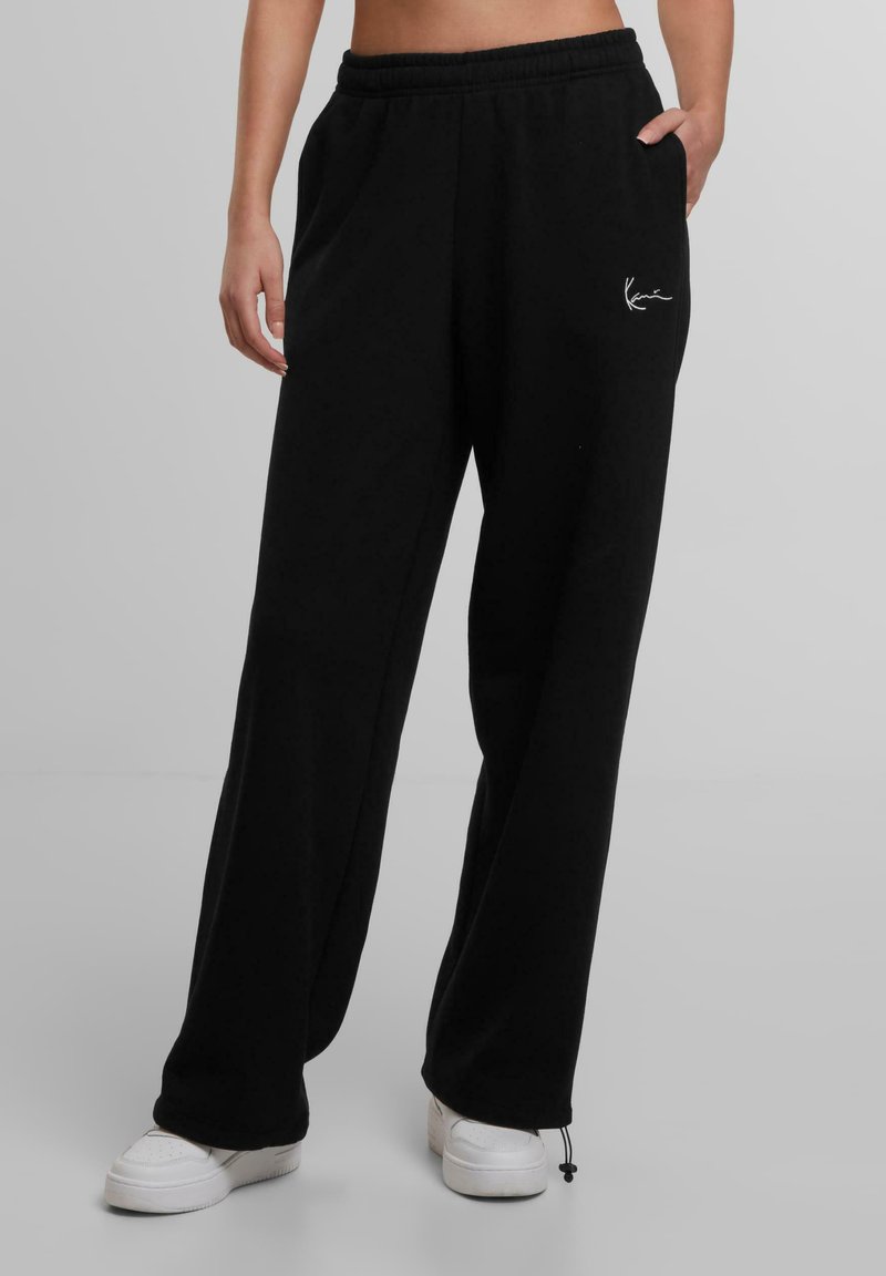 Schwarze Sweatpants in lockerer Passform mit elastischem Bund und Seitentaschen. Mit einem weißen Logo-Detail und leicht zulaufenden Knöcheln.