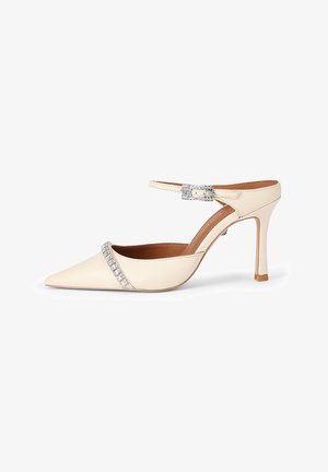 Chaussure en cuir beige à bout pointu avec une bride autour de la cheville et un détail en strass sur le devant. Elle présente un talon aiguille et une texture lisse.